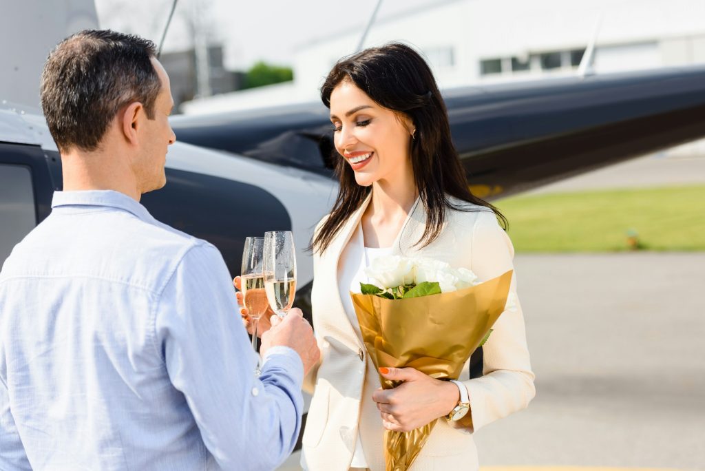 husband and wife clinking champagne glasses on romantic date near helicopter- The Best Aerial Activities You Can Do in Champagne with Champagne Curated Journeys - Exclusive Travel Representation, a luxury travel agency