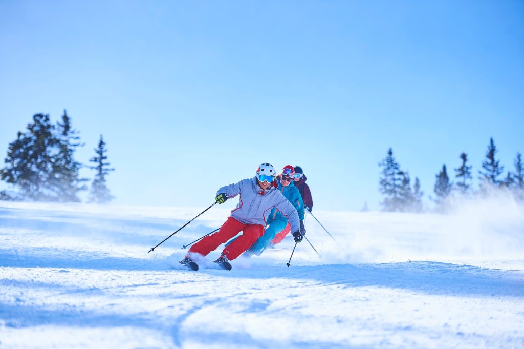 Row of male and female skiers skiing down snow covered ski slope | Experience the winter in luxury villas with exclusive skiing 