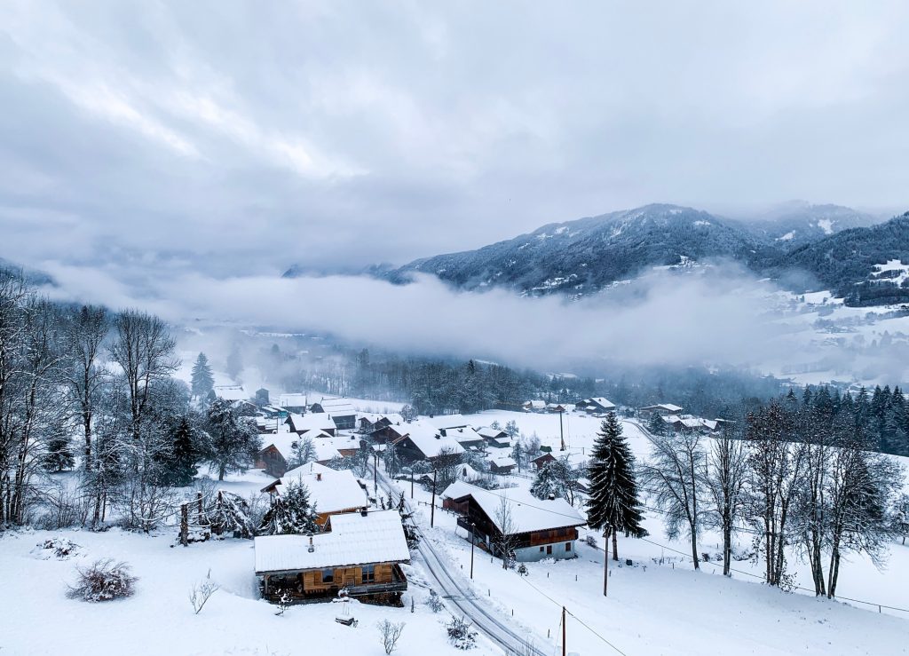 Snowy winter in french village in the Alps. Clouds below mountains, gloomy weather. Dusk.